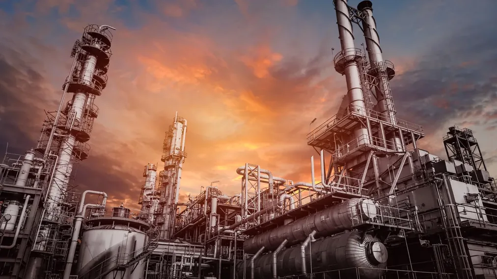 Refinaria iluminada ao entardecer com torres e tubulações